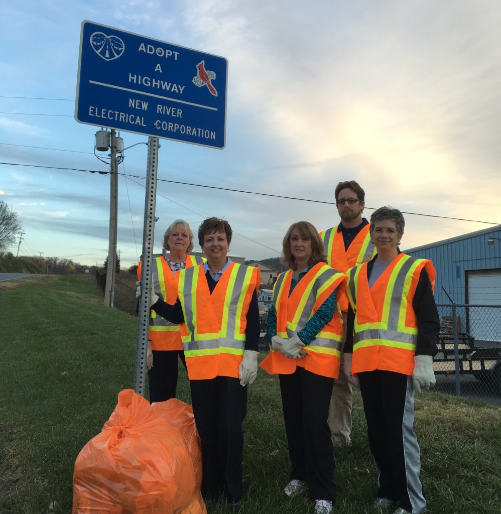 A group of NRE employees in orange vests cleaning up trash for Adopt A Highway.