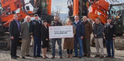 A group of individuals presenting a large donation check for $14,000 to the Virginia Military Institute, with construction equipment in the background.
