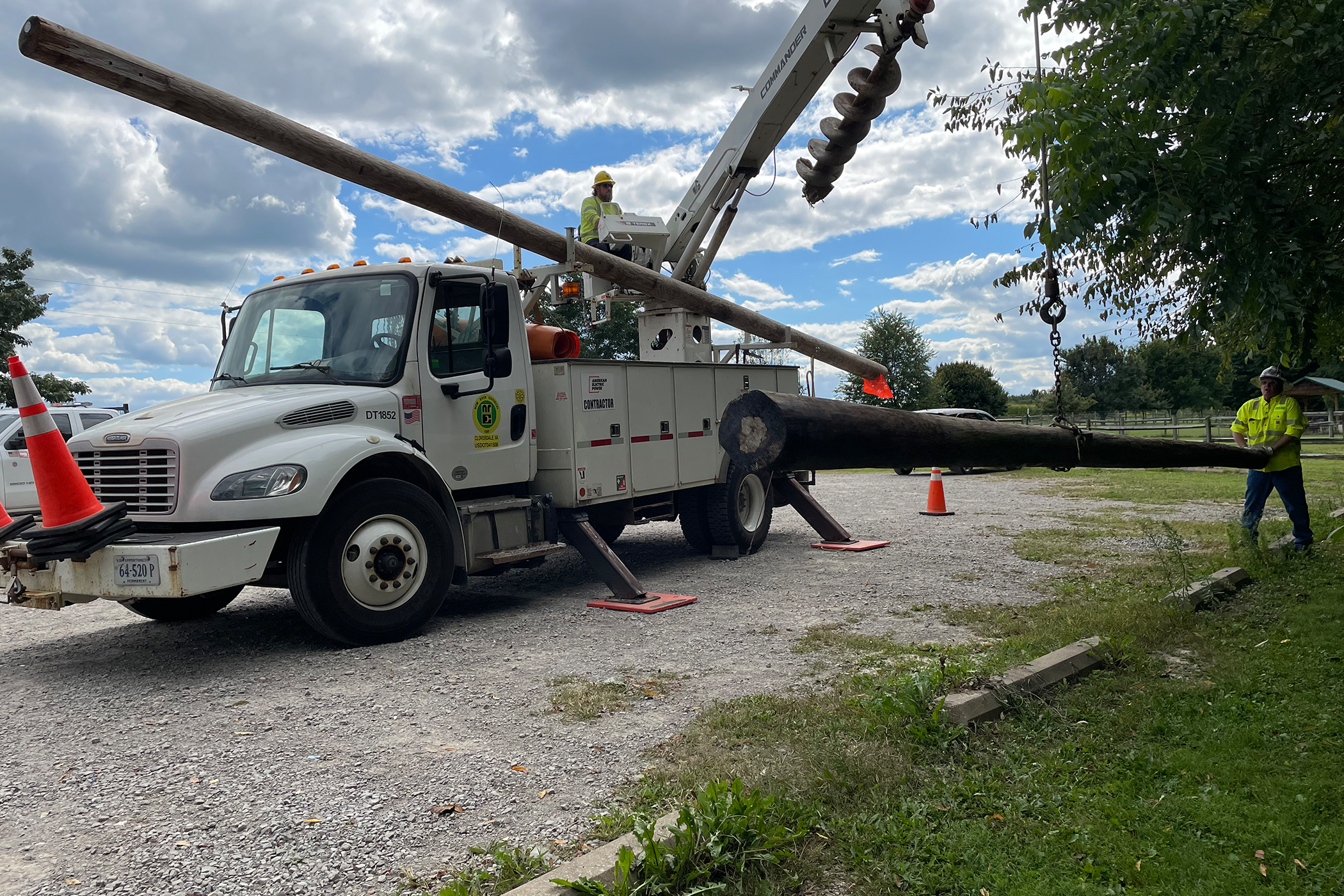 Two New River employees moving large wooden poles with a drill truck behind them.