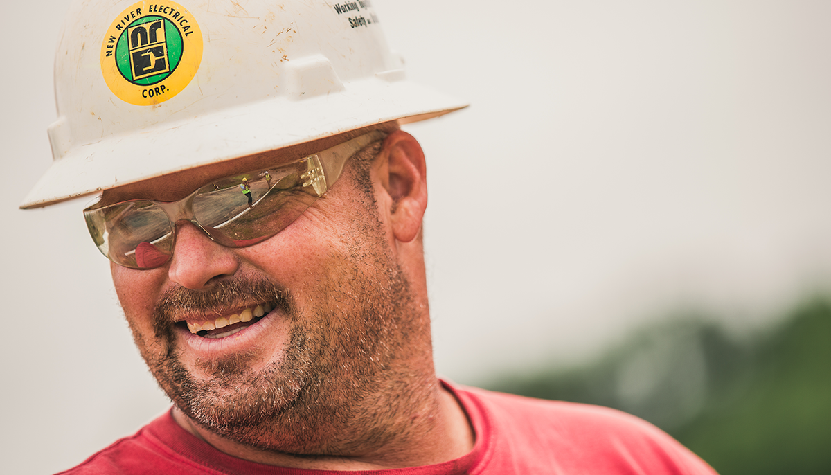 A New River Electrical employee in a red shirt and a white safety hat.