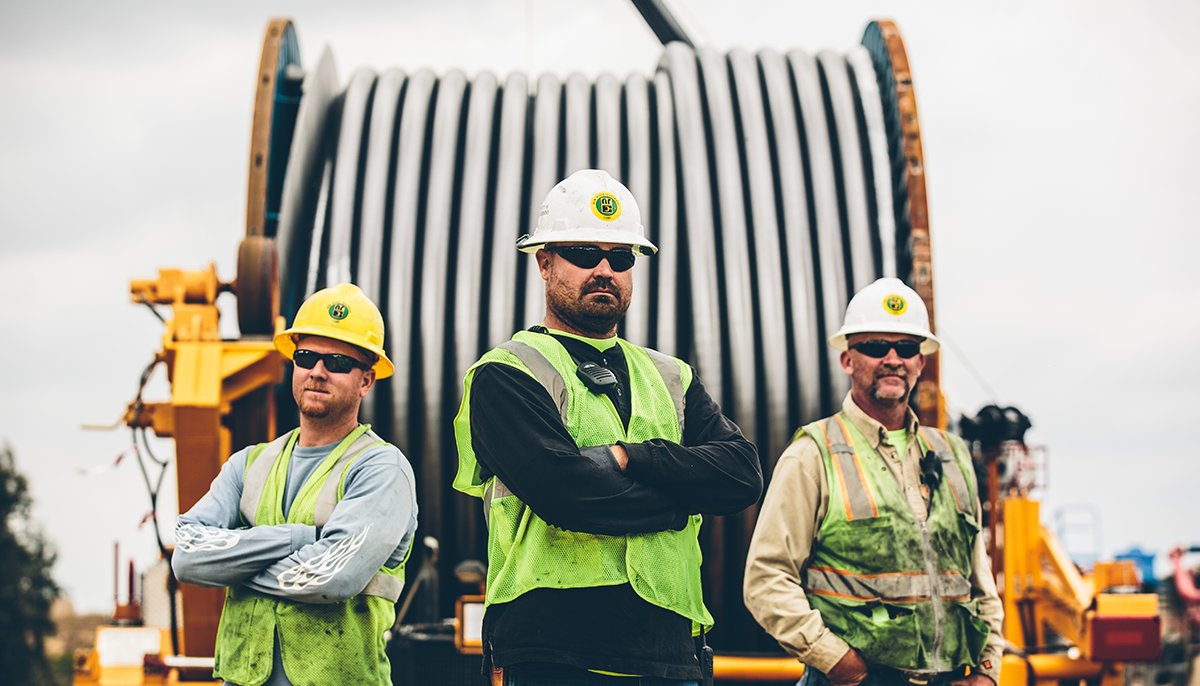 Three New River Electrical employee-owners standing in front of a large cable reel.