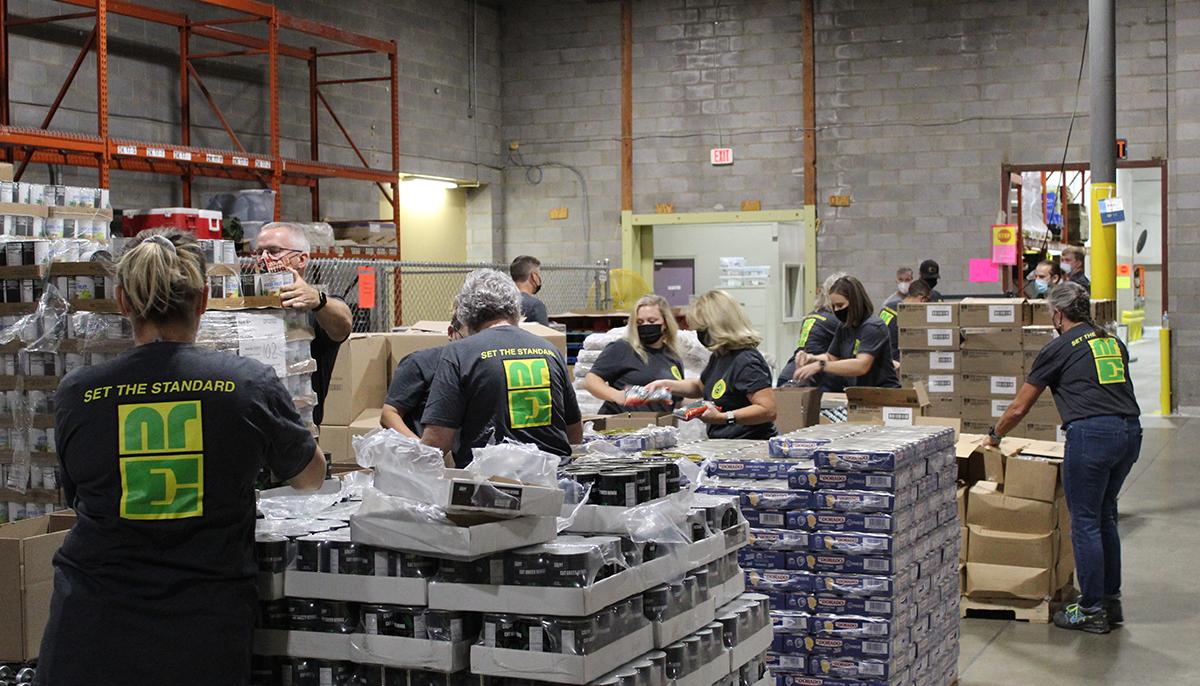 Group of people in a warehouse packing items, wearing matching shirts with New River ELectrical logo, 