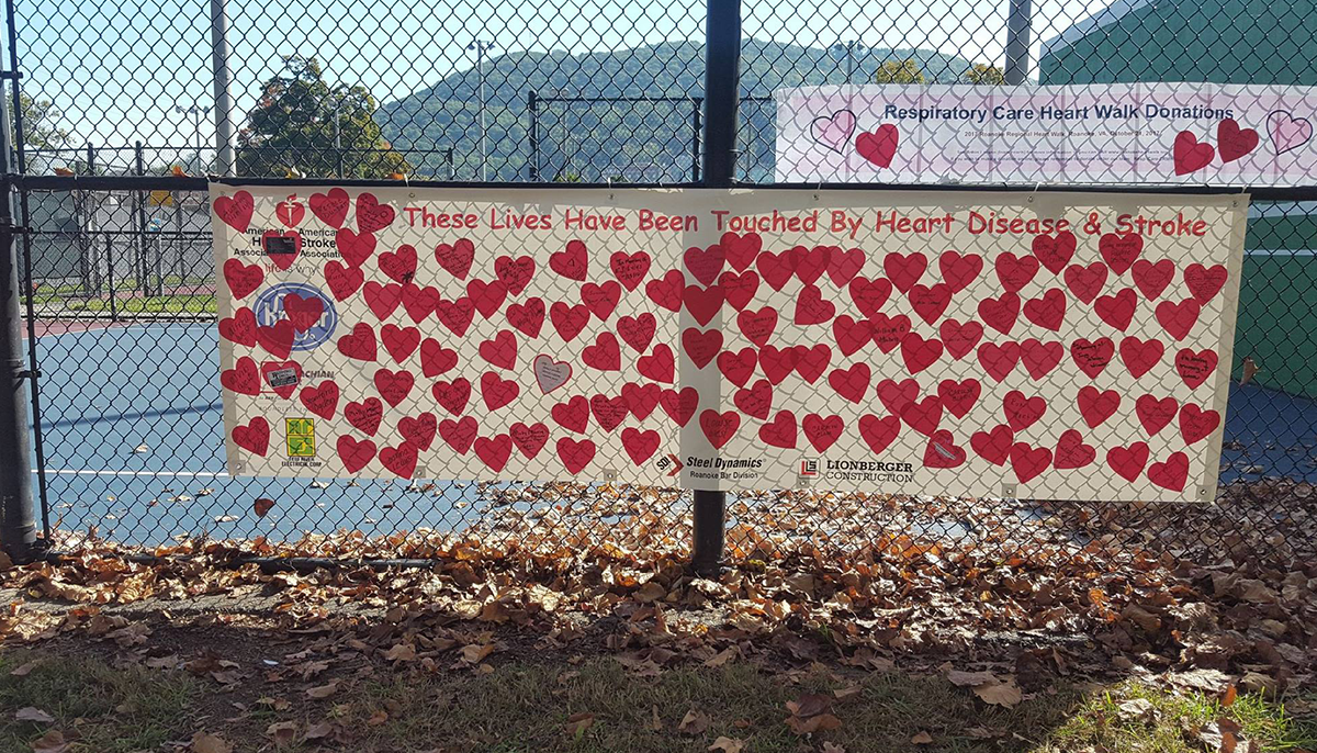A banner on a chain-link fence featuring many red hearts and the message 