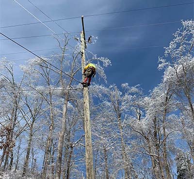 A New River Electrical Employee scaling a telephone pole to restore power in a snowstorm.