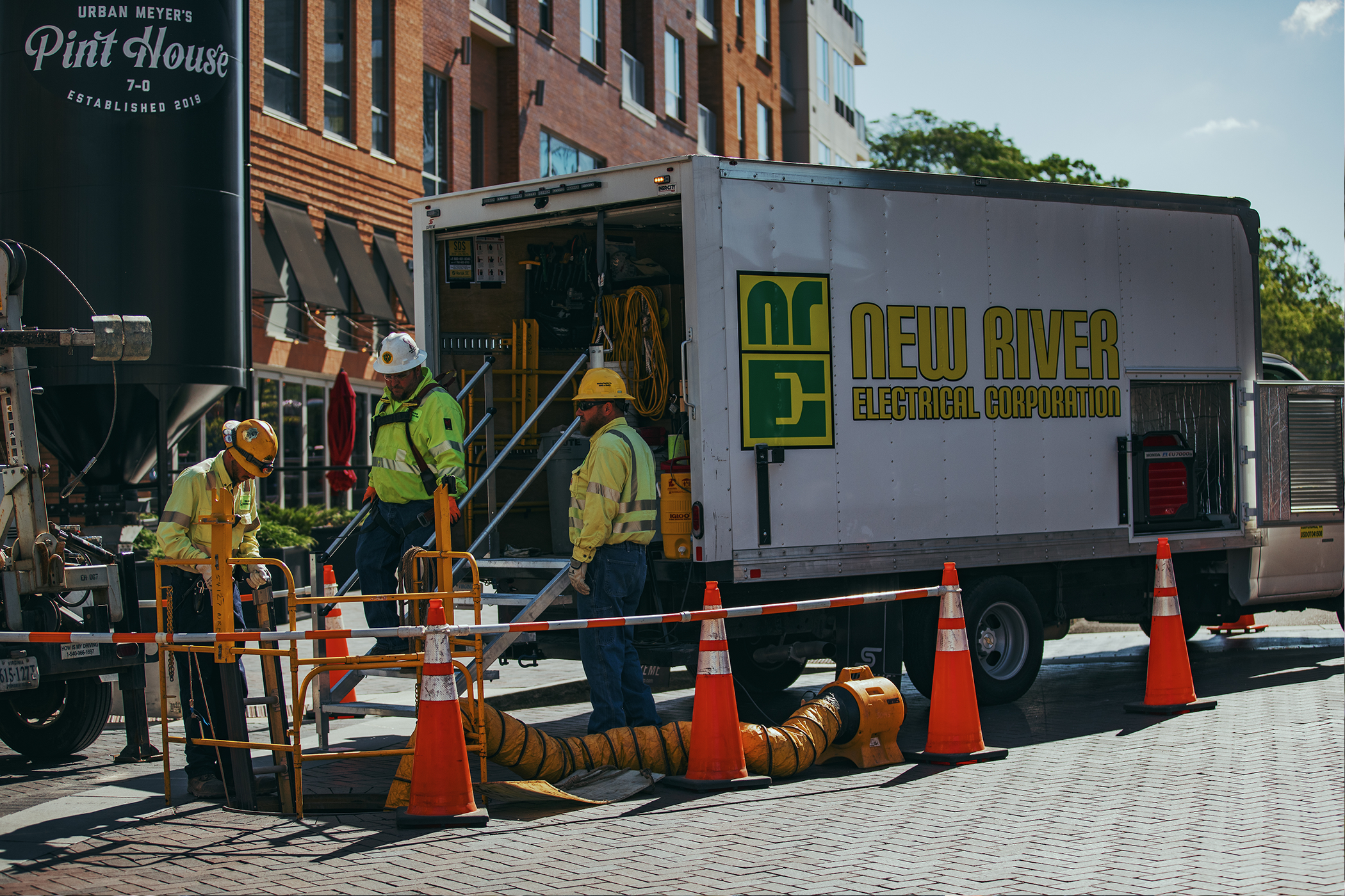 Three NRE employee looking down into a manhole with a NRE box truck sitting behind them.