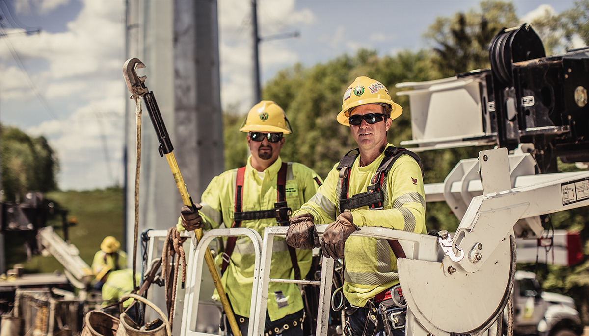 Two New River Employee-Owners standing in a bucket truck with safety equipment and yellow hook.