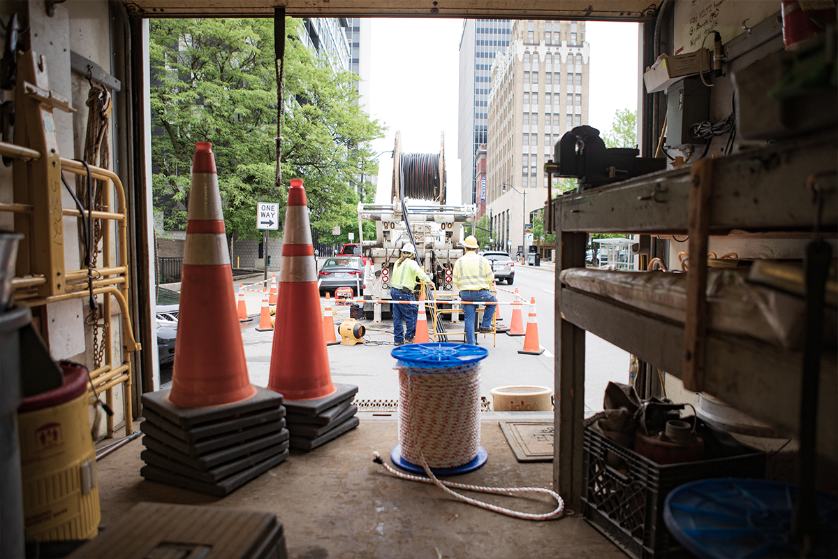 A view from the back of a NRE box truck with traffic cones, spools, and employees pulling cable out of a reel truck.