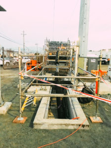 A construction site with a tall metal pole, safety barriers, and a deep trench with visible underground infrastructure.