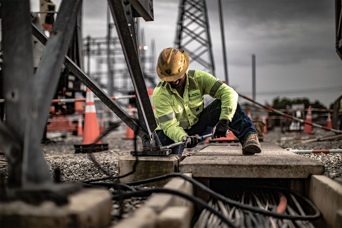 A New River Electrical employee working with a wrench on a metal structure with cables under him.