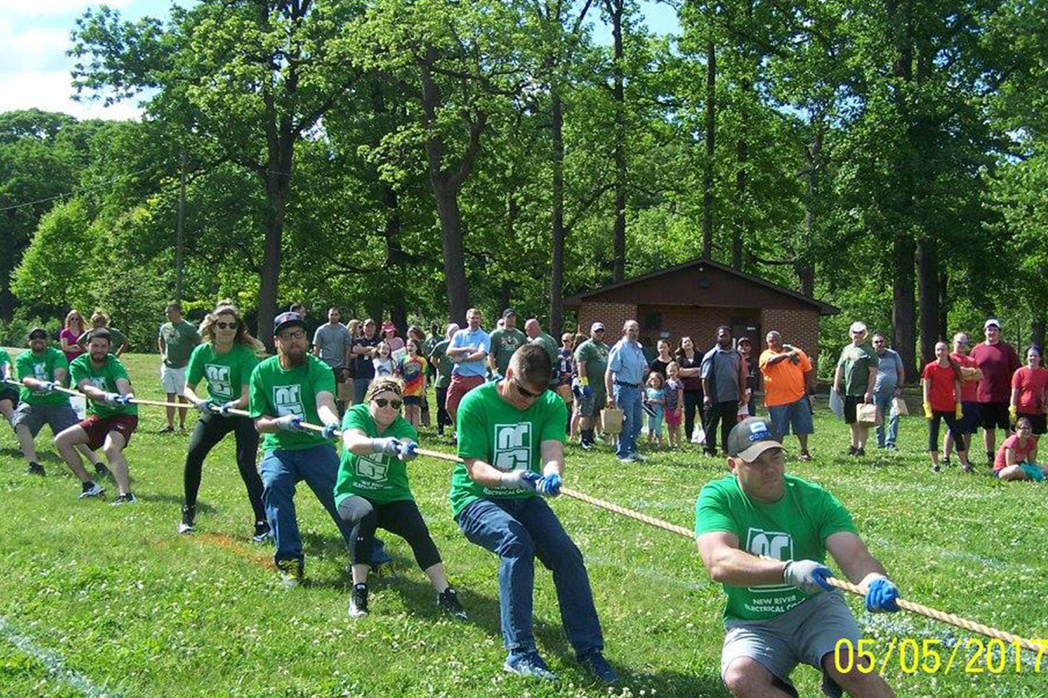 New River Electrical employees in green shirts pulling on a tug of war rope at tug for tots event.