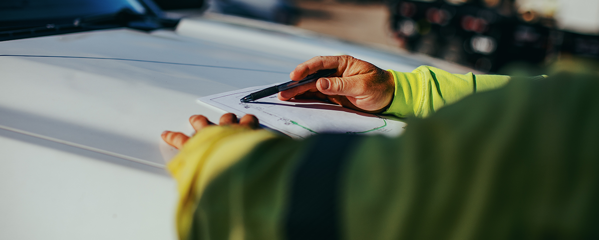 A NRE employee going over plans on a notebook on the hood of a white truck.