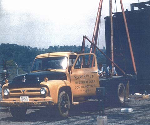Old photo of an early model yellow NRE work pickup truck at a job site