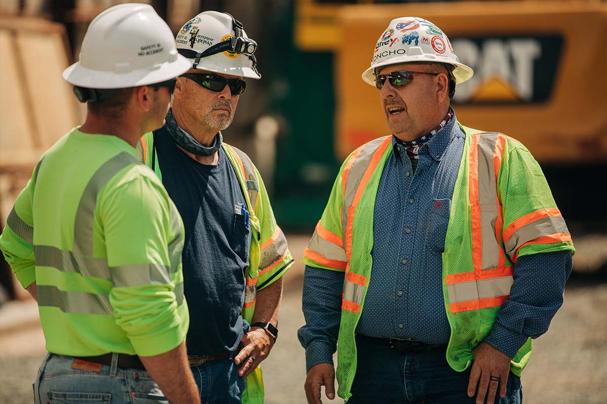 Three workers in hard hats having a discussion at a job site.