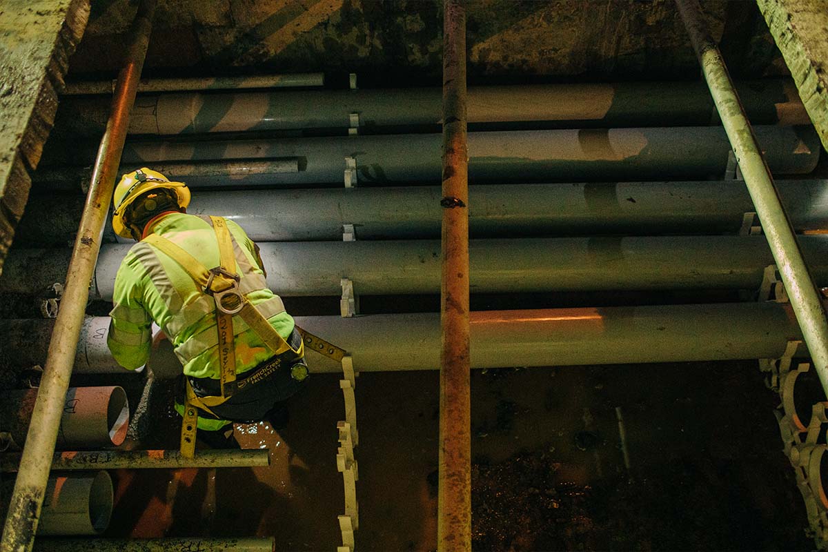 NRE employee crouched over an underground job site inspecting electrical pipe casings.