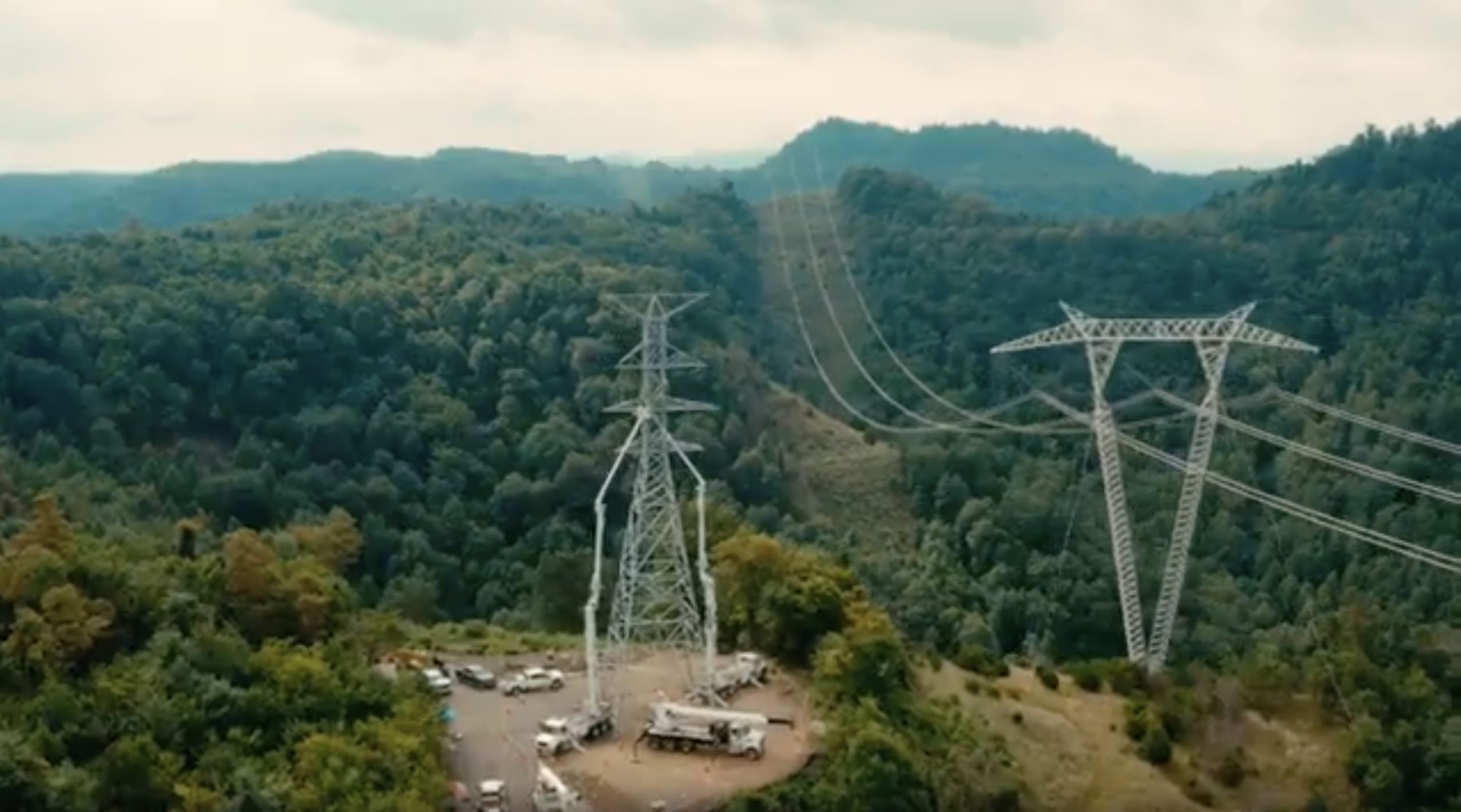 Aerial view of steel electrical towers and power lines running over a green forest