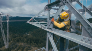 An NRE worker using a wrench on power lines high above ground