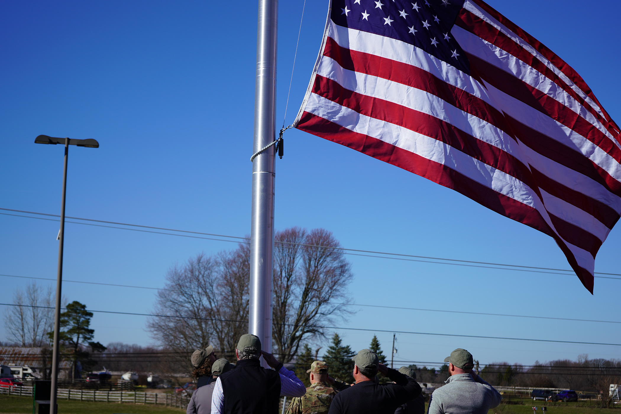 Shot from behind, a close up of men saluting the American flag as it flies half mast on a metal flagpole