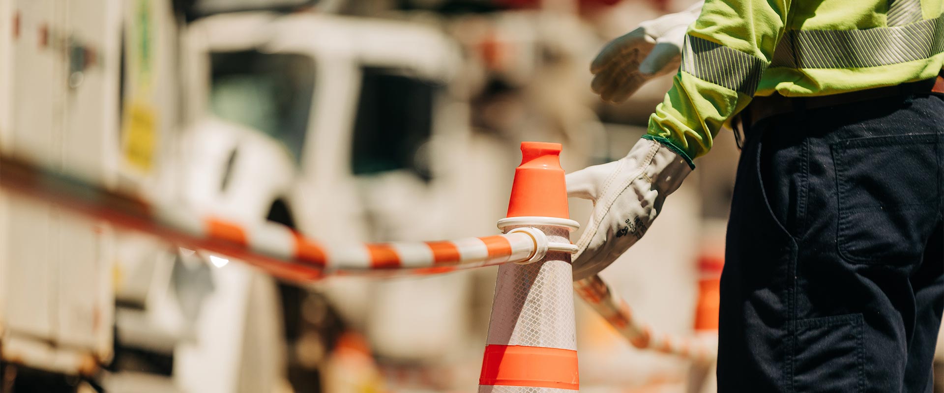 A white-gloved hand touching an orange safety cone connected to other orange safety cones by an orange and white cable