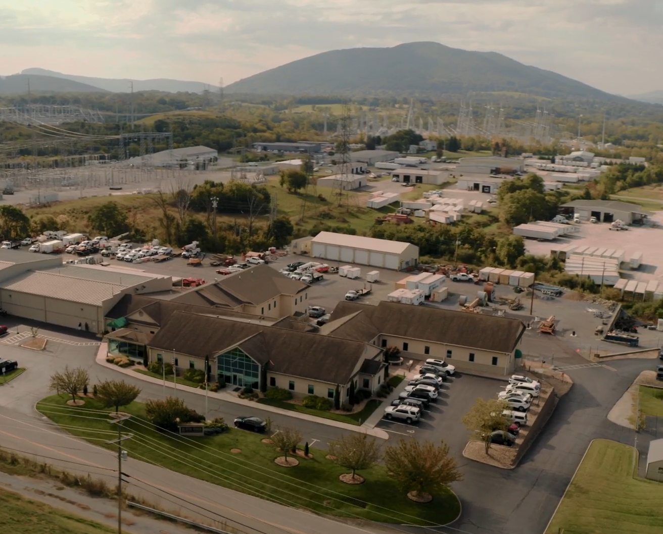 Aerial shot of a large building complex, surrounded by a parking lot. In the distance, an electrical grid stands tall against the backdrop of the Blue Ridge mountains.